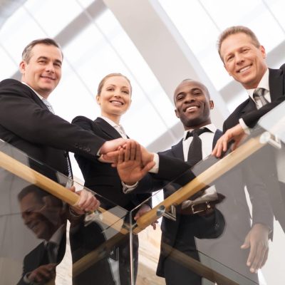 Strong business team. Low angle view of four confident business people standing close to each other and holding hands together